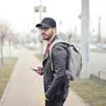 A fashionable young man in Budapest checking his smartphone on a busy street.